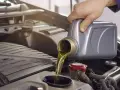 Main d'une personne versant de l'huile moteur d'un bidon gris dans le compartiment moteur d'une voiture. La question est : combien de litre huile moteur ?