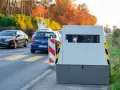 Un radar mobile de voiture surveille la route. Des voitures passent devant, dans un décor automnal.