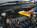 Main d'un mécanicien nettoyant le moteur d'une voiture avec un chiffon jaune, comme s'il utilisait un dégraissant moteur fait maison.