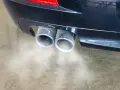Double sortie d'échappement d'une voiture émettant de la fumée. Une odeur d'échappement dans l'habitacle peut être un signe de problème.