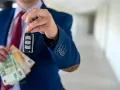Un homme en costume tient une clé de voiture et des billets en euros. La question est : peut-on payer une voiture en liquide ?