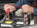 Mains pour recharger batterie voiture avec des câbles de démarrage. Les pinces rouges sont connectées à la batterie.
