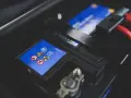 Gros plan sur une batterie de voiture, avec des symboles de sécurité et des câbles rouges. L'image évoque la durée de vie batterie voiture.