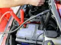 Comment utiliser un booster de batterie : des câbles rouges et noirs sont connectés à une batterie de voiture pour la démarrer.
