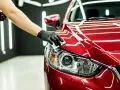 Main d'une personne gantée appliquant un produit sur le phare d'une voiture rouge. Une astuce de grand-mère pour faire briller une voiture.