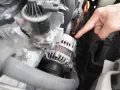 Main d'un mécanicien pointant vers l'alternateur pour tester un régulateur de tension dans un compartiment moteur.