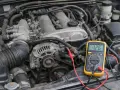 Multimètre jaune branché sur un moteur de voiture. L'écran affiche 12.6V, une mesure pour savoir si une batterie ne tient plus la charge.