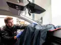 Un technicien en lunettes de protection utilise une housse pour protéger le tableau de bord lors d'une intervention sur la commande de désembuage.
