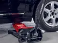 Un cric hydraulique rouge est positionné pour soulever une voiture. Il est essentiel de savoir ou placer le cric sous la voiture pour un changement de roue sûr.