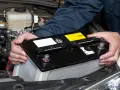 Maintenant, le démontage de la batterie de voiture est en cours. Les mains d'un mécanicien retirent la batterie noire du compartiment moteur.