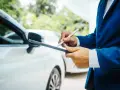 Un homme en costume bleu utilise une tablette pour évaluer la valeur vénale d'un véhicule blanc.
