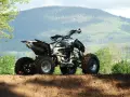 Quad tout-terrain, prêt pour son contrôle technique, avec des pneus boueux et un paysage montagneux en arrière-plan.