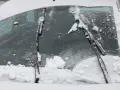 Pare-brise enneigé, un essuie-glace bloqué au milieu, prêt à dégager la vue.