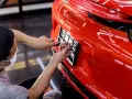 Un homme installe une plaque allemande voiture sur un véhicule rouge vif.