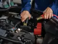 Mains de mécanicien effectuant le branchement batterie voiture avec des câbles de démarrage.