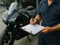 Un technicien remplit une liste pour le contrôle technique d'une mobylette noire, assurant sa sécurité.