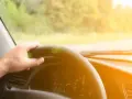 Main d'un conducteur tenant le volant d'une voiture qui tremble au point mort, sous un soleil éclatant.