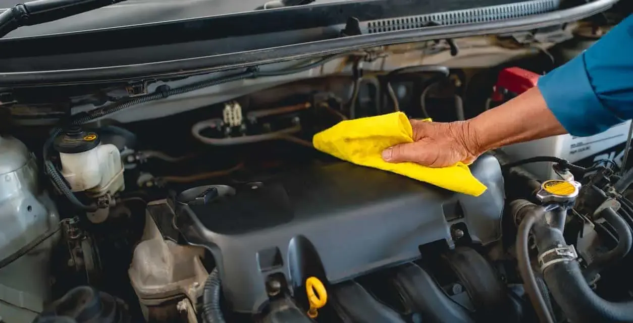 Main d'un mécanicien nettoyant le moteur d'une voiture avec un chiffon jaune, comme s'il utilisait un dégraissant moteur fait maison.