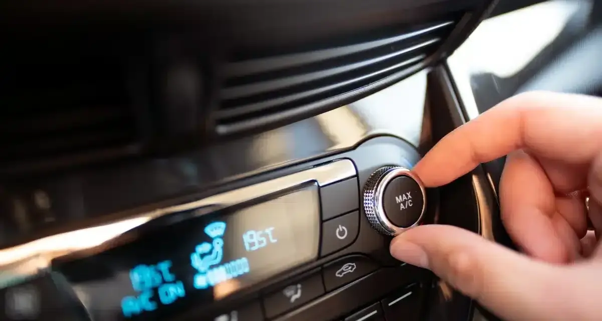 Main de conducteur ajustant le bouton "MAX A/C" sur le tableau de bord. Faut-il laisser la climatisation voiture en permanence ?