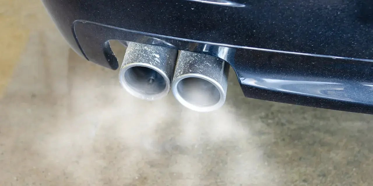 Double sortie d'échappement d'une voiture émettant de la fumée. Une odeur d'échappement dans l'habitacle peut être un signe de problème.