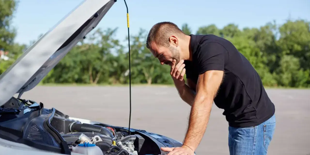Homme désemparé devant le moteur de sa voiture, capot ouvert. Il semble avoir une panne batterie.