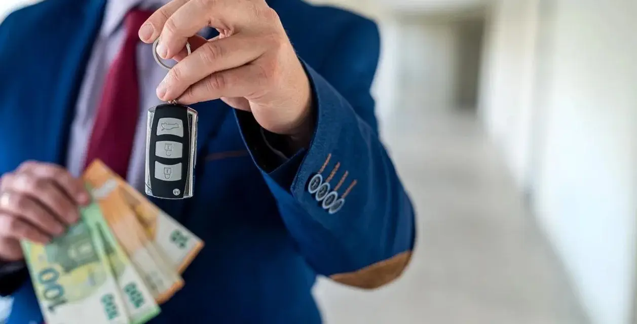 Un homme en costume tient une clé de voiture et des billets en euros. La question est : peut-on payer une voiture en liquide ?