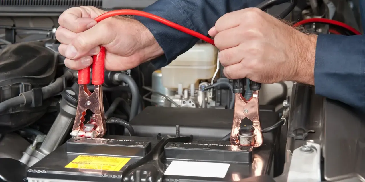 Mains pour recharger batterie voiture avec des câbles de démarrage. Les pinces rouges sont connectées à la batterie.