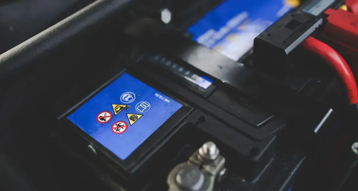 Gros plan sur une batterie de voiture, avec des symboles de sécurité et des câbles rouges. L'image évoque la durée de vie batterie voiture.