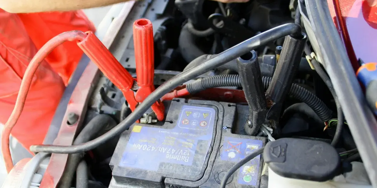 Comment utiliser un booster de batterie : des câbles rouges et noirs sont connectés à une batterie de voiture pour la démarrer.