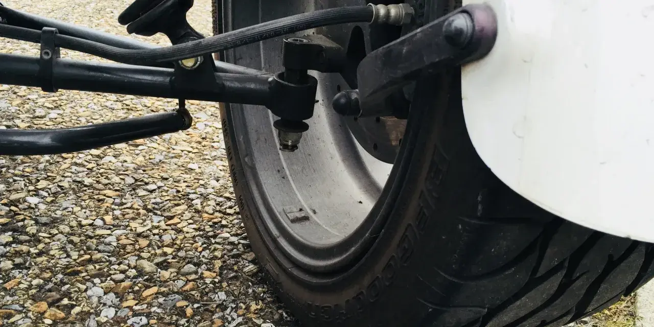 Gros pneu de véhicule sur un chemin de gravier. Le système de suspension et de direction est visible. J'espère que mes pneus font du bruit quand je roule, car cela pourrait indiquer un problème.