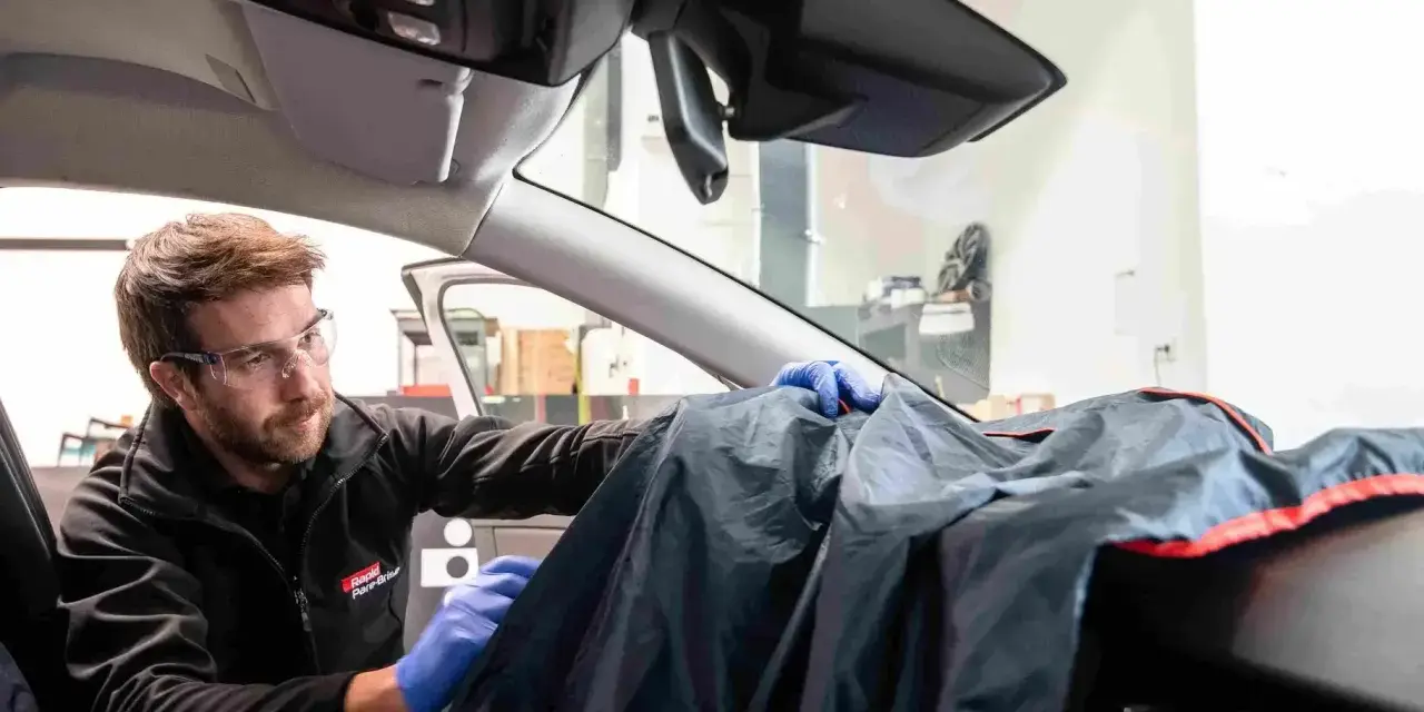 Un technicien en lunettes de protection utilise une housse pour protéger le tableau de bord lors d'une intervention sur la commande de désembuage.
