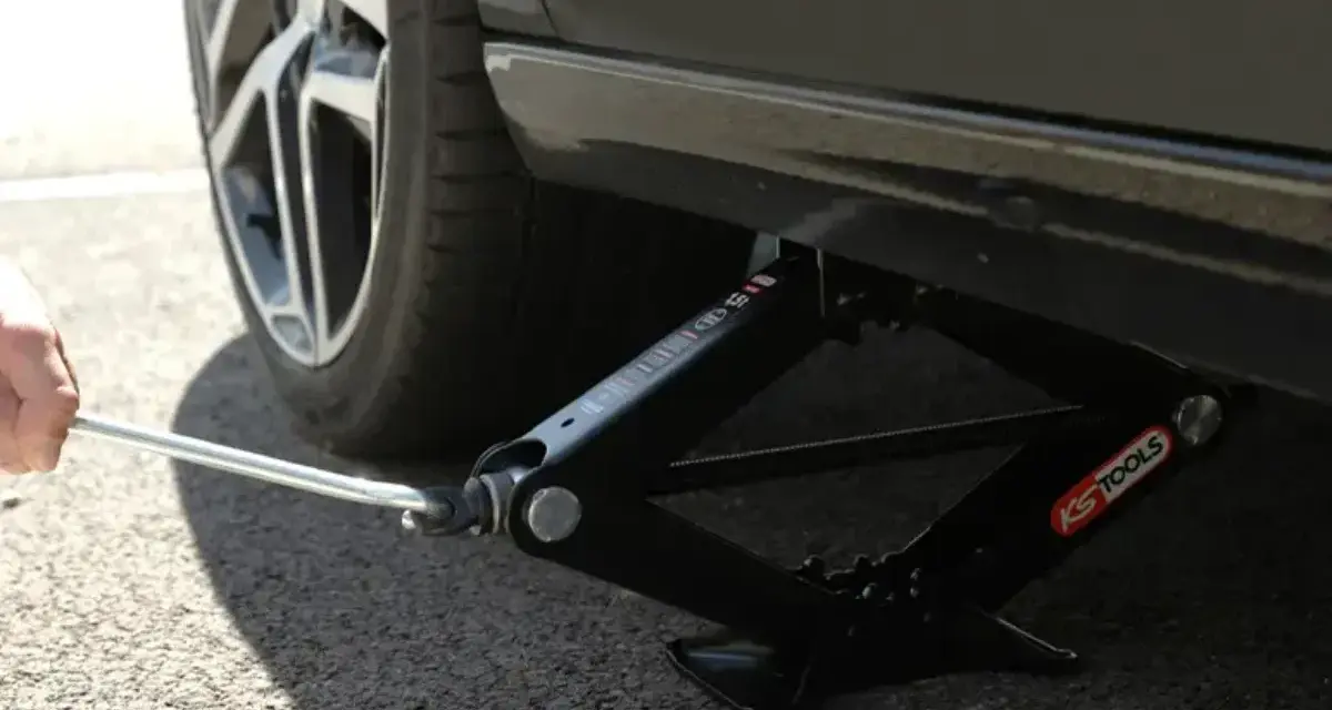Utilisation d'un cric en ciseaux pour trouver le bon point de levage voiture. La roue est visible.