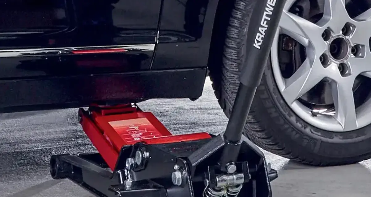 Un cric hydraulique rouge est positionné pour soulever une voiture. Il est essentiel de savoir ou placer le cric sous la voiture pour un changement de roue sûr.
