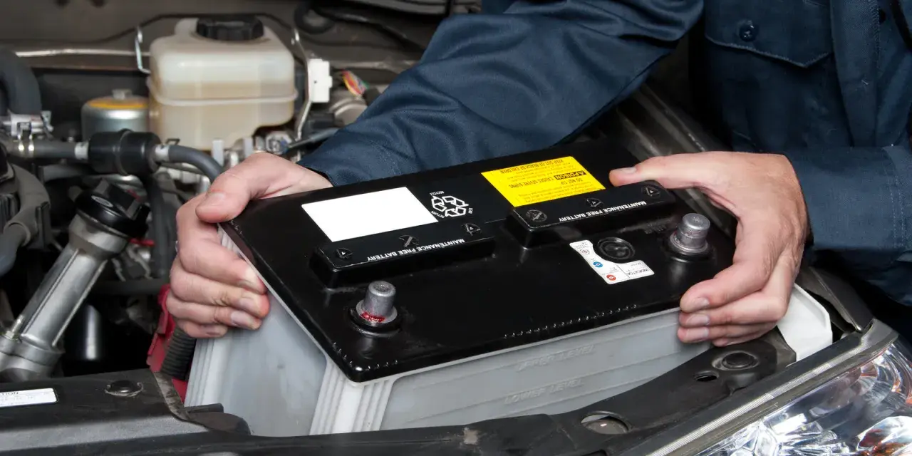 Maintenant, le démontage de la batterie de voiture est en cours. Les mains d'un mécanicien retirent la batterie noire du compartiment moteur.