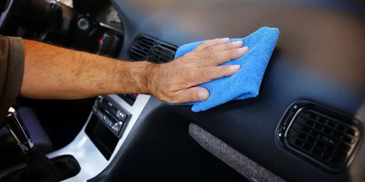 Main d'homme nettoyant le tableau de bord d'une voiture avec un chiffon bleu. Un nettoyant plastique voiture fait maison pour un intérieur impeccable.