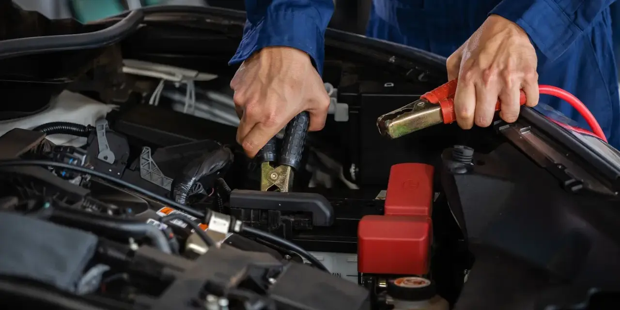 Mains de mécanicien effectuant le branchement batterie voiture avec des câbles de démarrage.