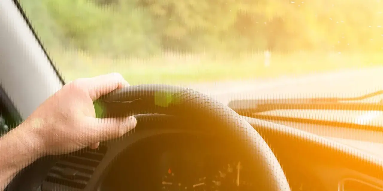 Main d'un conducteur tenant le volant d'une voiture qui tremble au point mort, sous un soleil éclatant.