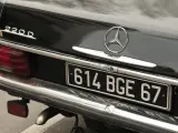 Arrière d'une Mercedes 220D noire. La plaque d'immatriculation "614 BGE 67" est visible. Pour savoir les chevaux de ma voiture, il faut regarder la carte grise.