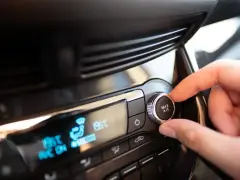 Main de conducteur ajustant le bouton "MAX A/C" sur le tableau de bord. Faut-il laisser la climatisation voiture en permanence ?