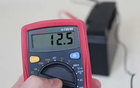 Multimètre affichant 12.5V, indiquant une batterie déchargée ou morte.