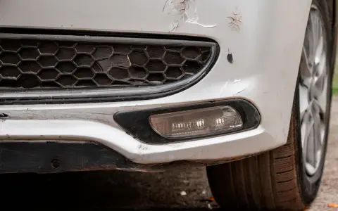 Pare-chocs avant d'une voiture blanche avec des éraflures et des éclats de peinture. Une méthode pour redresser carrosserie eau chaude pourrait aider à réparer ces dommages.
