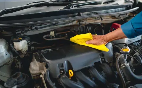 Main d'un mécanicien nettoyant le moteur d'une voiture avec un chiffon jaune, comme s'il utilisait un dégraissant moteur fait maison.