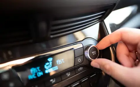 Main de conducteur ajustant le bouton "MAX A/C" sur le tableau de bord. Faut-il laisser la climatisation voiture en permanence ?