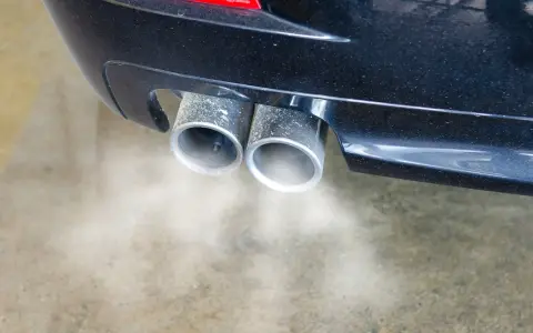 Double sortie d'échappement d'une voiture émettant de la fumée. Une odeur d'échappement dans l'habitacle peut être un signe de problème.