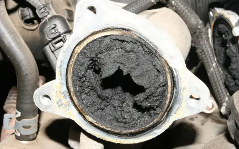 Gros dépôt de suie noire obstruant une vanne EGR, signe d'un défaut potentiel.