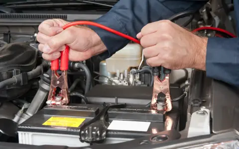 Mains pour recharger batterie voiture avec des câbles de démarrage. Les pinces rouges sont connectées à la batterie.