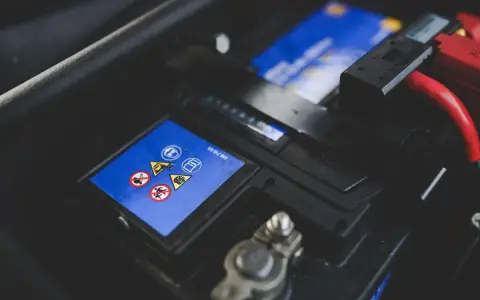 Gros plan sur une batterie de voiture, avec des symboles de sécurité et des câbles rouges. L'image évoque la durée de vie batterie voiture.