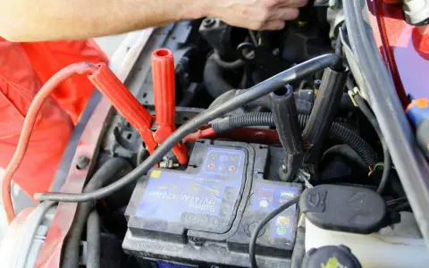 Comment utiliser un booster de batterie : des câbles rouges et noirs sont connectés à une batterie de voiture pour la démarrer.