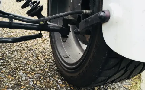 Gros pneu de véhicule sur un chemin de gravier. Le système de suspension et de direction est visible. J'espère que mes pneus font du bruit quand je roule, car cela pourrait indiquer un problème.