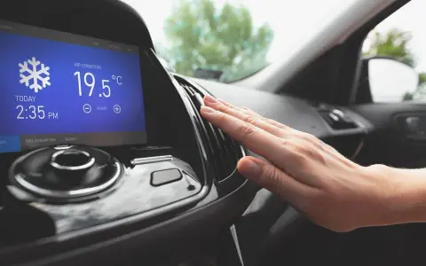 Main d'une personne vérifiant la sortie d'air climatisé dans une voiture, affichant 19.5°C. Parfait pour le clim air chaud.